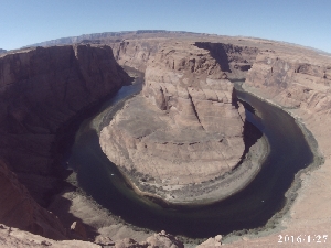 Vue aérienne spectaculaire du Serpent de l'Eau (Colorado River) dans le Grand Canyon du Colorado. L'eau sinueuse forme un grand cercle, entourée de falaises rouges et brunes. Le ciel est clair et bleu.